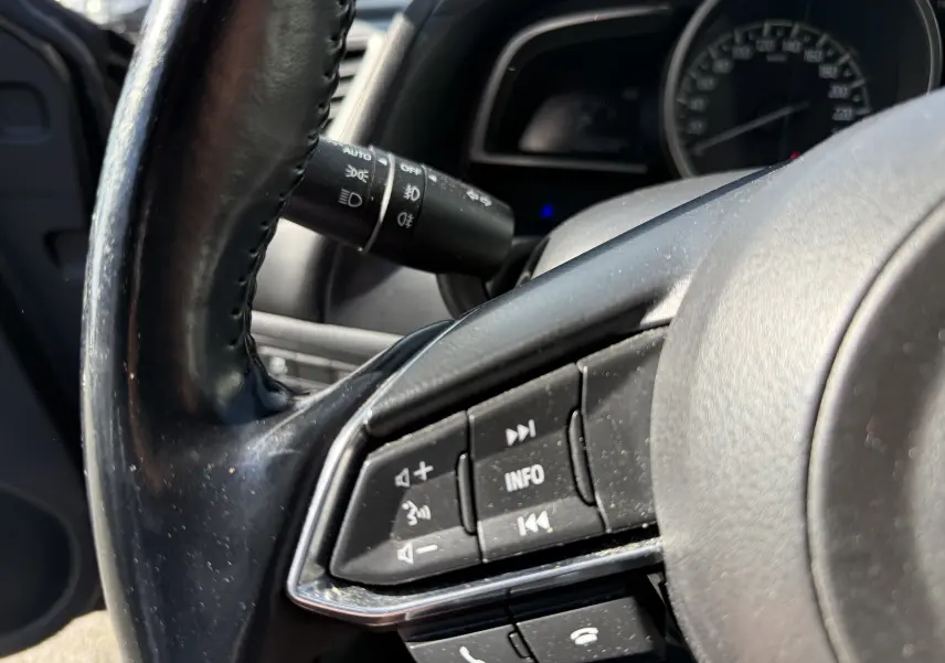 Gros plan sur le volant côté gauche d'une Mazda3 2017, montrant les commandes audio et téléphone intégrées.