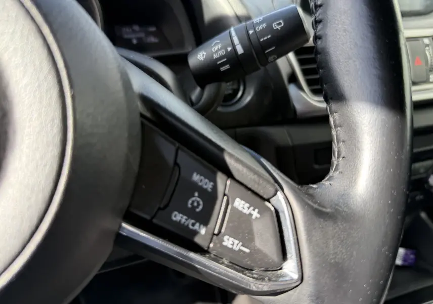 Gros plan sur les commandes du régulateur de vitesse au volant en cuir noir de la Mazda3 gris 2017.