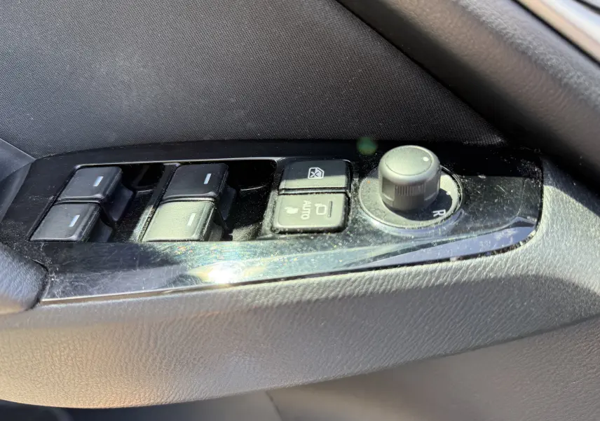 Gros plan sur les commandes de lève-vitres et réglage des rétroviseurs côté gauche d’une Mazda3 gris 2017.