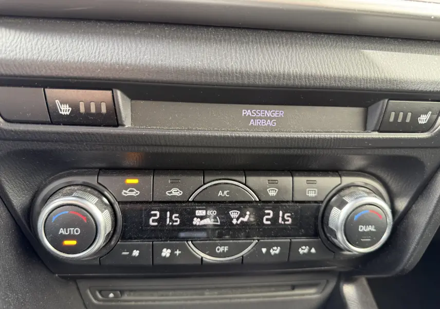 Vue rapprochée du tableau de bord de la Mazda3 gris 2017, montrant la climatisation automatique bi-zone et les commandes chauffantes.