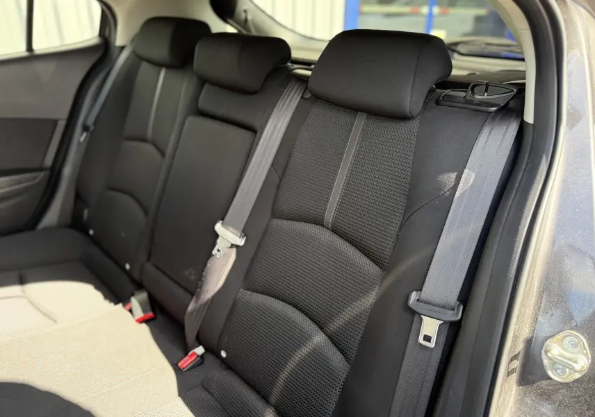 Vue intérieure sur les sièges arrière en tissu noir de la Mazda3 gris 2017, avec ceintures de sécurité visibles.