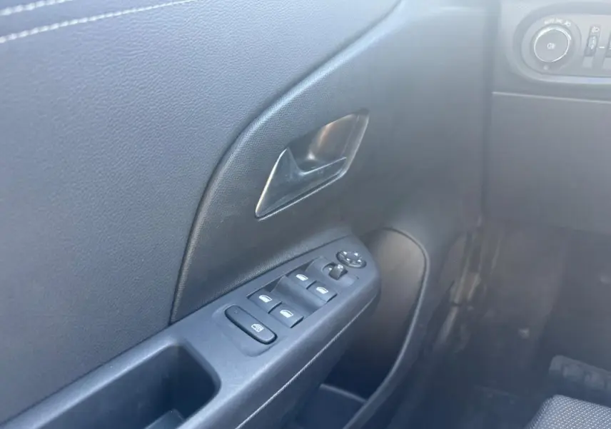 Vue rapprochée de la porte avant gauche intérieure de l’Opel Corsa rouge, avec commandes des vitres électriques et poignée noire.