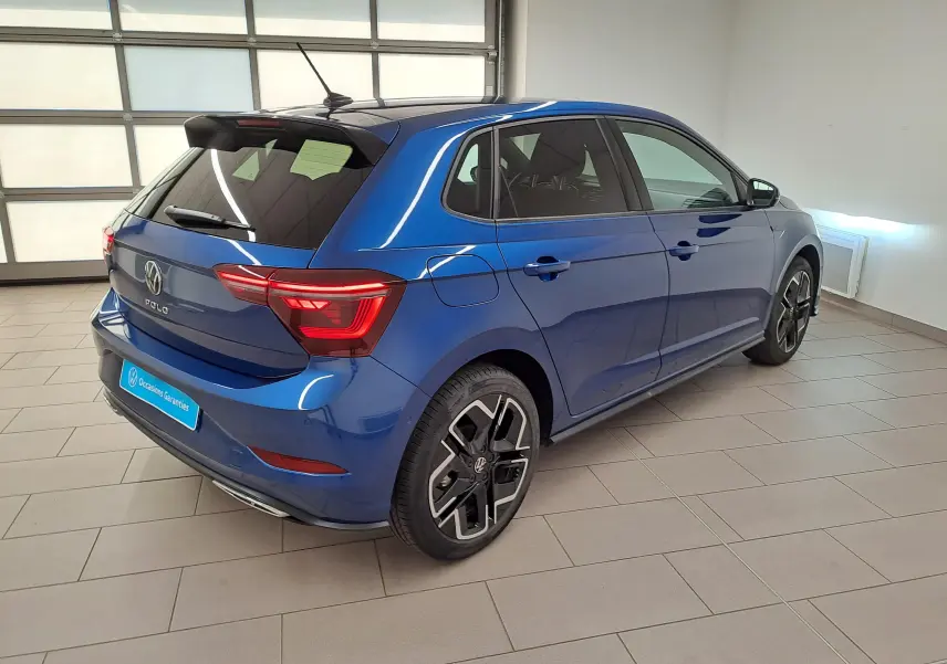 Vue 3/4 arrière droite d'une Volkswagen Polo Bleu Récif métallisée avec jantes noires et toit noir en intérieur showroom.