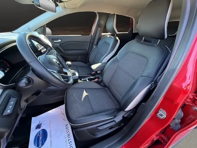 Intérieur avant droit du Renault Captur rouge 2024, sièges tissu gris avec coutures blanches et tableau de bord moderne.