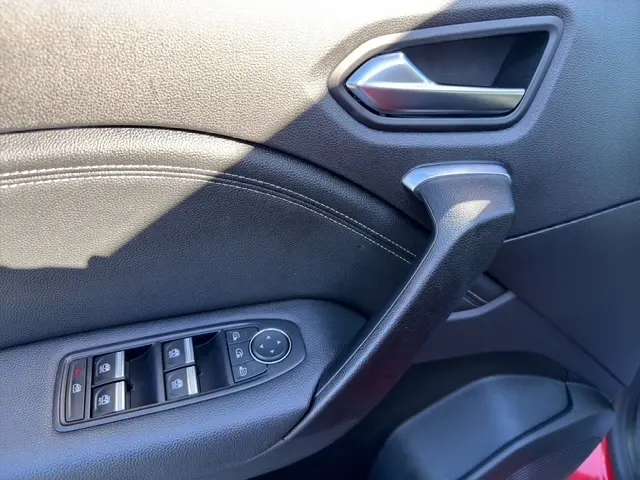 Détail de la porte avant gauche intérieure d’un Renault Captur rouge 2024, avec commandes des vitres et poignée noire.