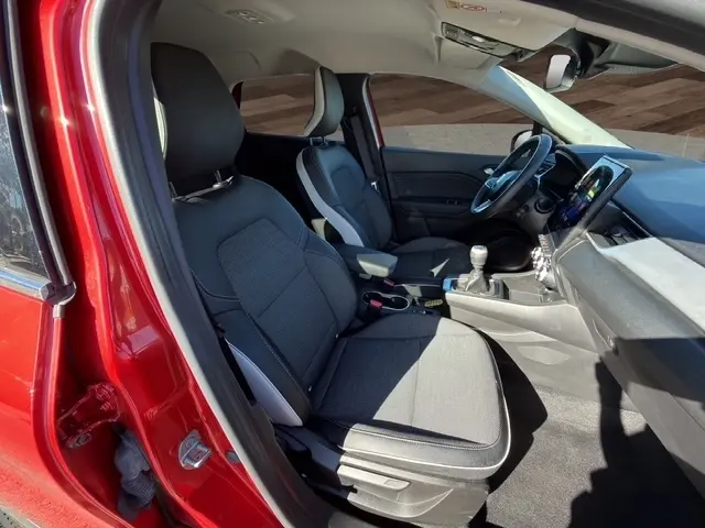 Vue intérieure côté conducteur du Renault Captur rouge 2024, montrant les sièges, le volant multifonctions et la console avec boîte manuelle.