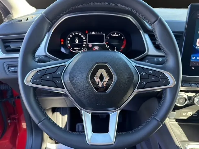 Vue centrée sur le volant noir du Renault Captur rouge 2024, avec tableau de bord numérique et commandes multifonctions visibles.