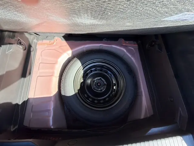 Vue plongeante sur la roue de secours noire logée dans le coffre rouge du Renault Captur Techno TCe 90 2024.