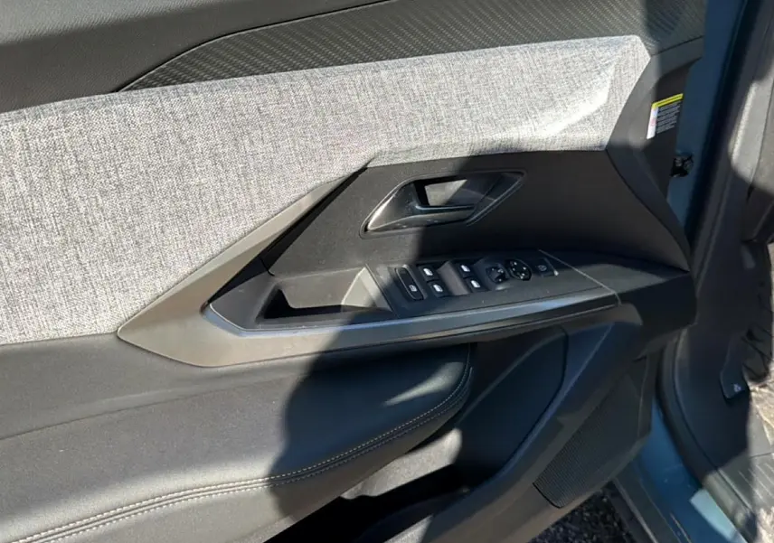 Vue intérieure côté gauche de la porte avant d’un Peugeot 3008 bleu Ingara avec garniture tissu et commandes électriques.
