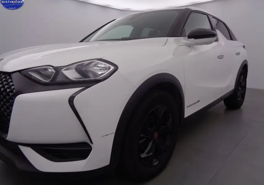Vue 3/4 avant droit d'un DS3 Crossback blanc banquise avec jantes noires et calandre distinctive en losange.