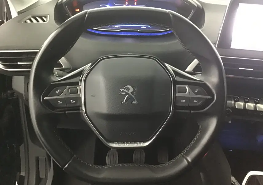 Vue rapprochée du volant cuir noir du Peugeot 5008 2019 avec commandes intégrées et tableau de bord digital bleu.
