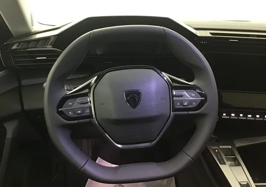 Vue rapprochée du volant cuir noir du Peugeot 308 gris Artense, avec commandes intégrées et tableau de bord moderne.