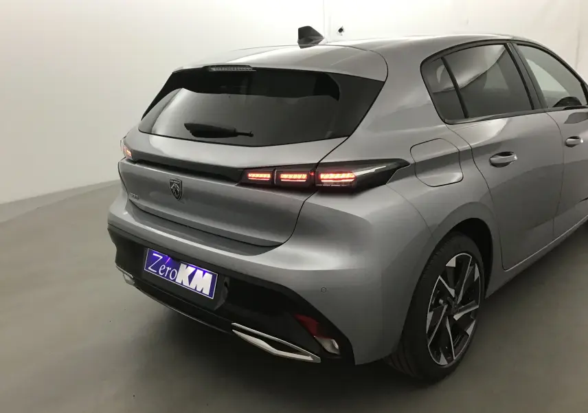 Vue 3/4 arrière droite d'une Peugeot 308 gris Artense avec feux arrière allumés et jantes alliage noires.