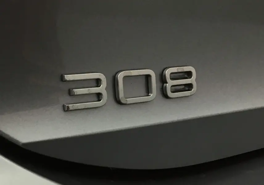 Gros plan sur l’inscription 308 en chrome sur la carrosserie gris artense d’une Peugeot 308.