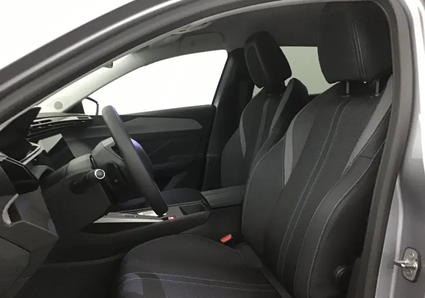 Intérieur de la Peugeot 308 gris Artense, vue côté conducteur, sièges en tissu avec surpiqûres contrastées et volant cuir.