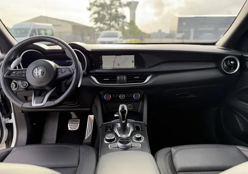 Intérieur noir de l'Alfa Romeo Stelvio 2023, vue frontale du tableau de bord avec écran de navigation et volant multifonction.
