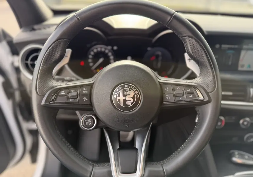 Vue rapprochée du volant en cuir noir de l'Alfa Romeo Stelvio 2023 avec logo central et commandes intégrées.