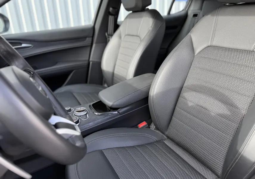 Intérieur de l'Alfa Romeo Stelvio 2023, vue côté conducteur sur les sièges en cuir gris et la console centrale.