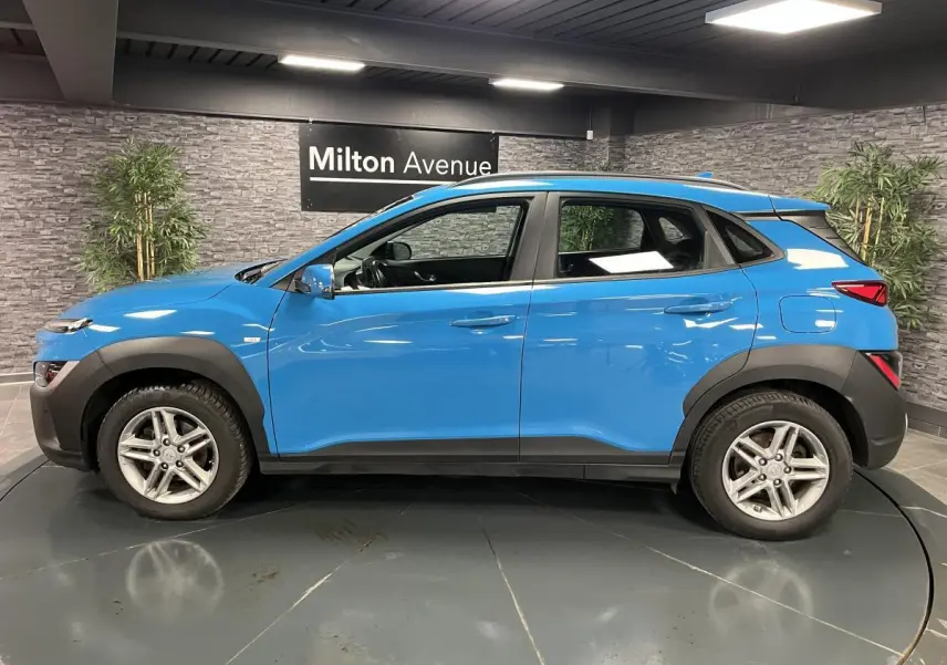 Vue de profil côté gauche d'un Hyundai Kona 1.6 CRDi Hybrid 48V bleu avec protections noires et jantes alliage 16 pouces.