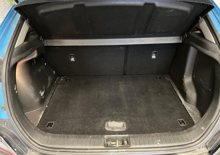 Coffre ouvert vu de l'arrière d'un Hyundai Kona bleu, montrant un espace de chargement propre et spacieux.