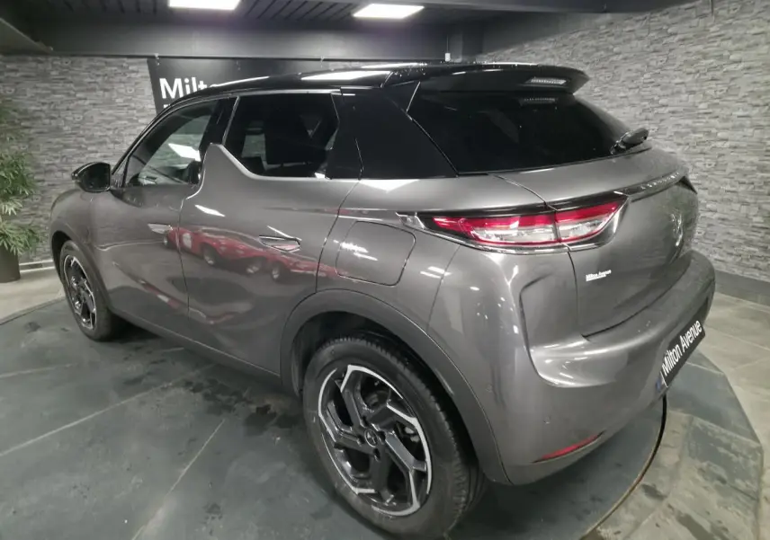 Vue 3/4 arrière droite du DS3 Crossback gris métallisé avec toit noir et jantes alliage 18 pouces en intérieur showroom.