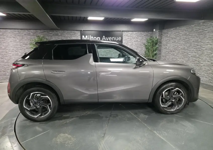 Vue latérale droite d'un DS3 Crossback gris métallisé avec toit noir et jantes alliage 18 pouces dans un showroom.