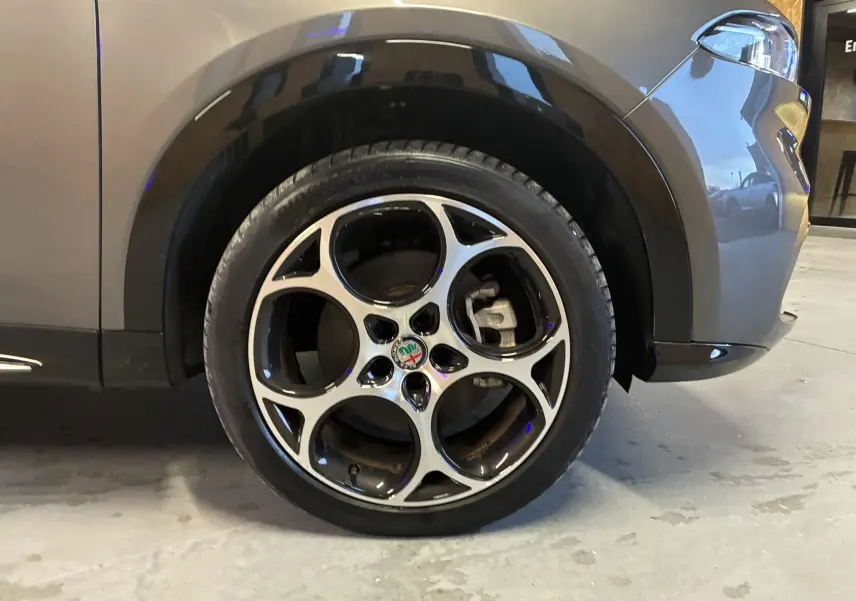 Gros plan sur la roue avant droite gris foncé de l'Alfa Romeo Tonale 1.3 PHEV 280 BVA TI avec jante distinctive à cinq cercles.