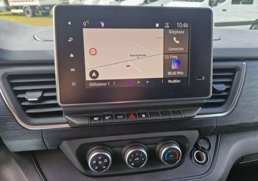 Vue rapprochée du tableau de bord du Nissan Primastar blanc 2025, mettant en valeur l’écran tactile et les commandes de climatisation.