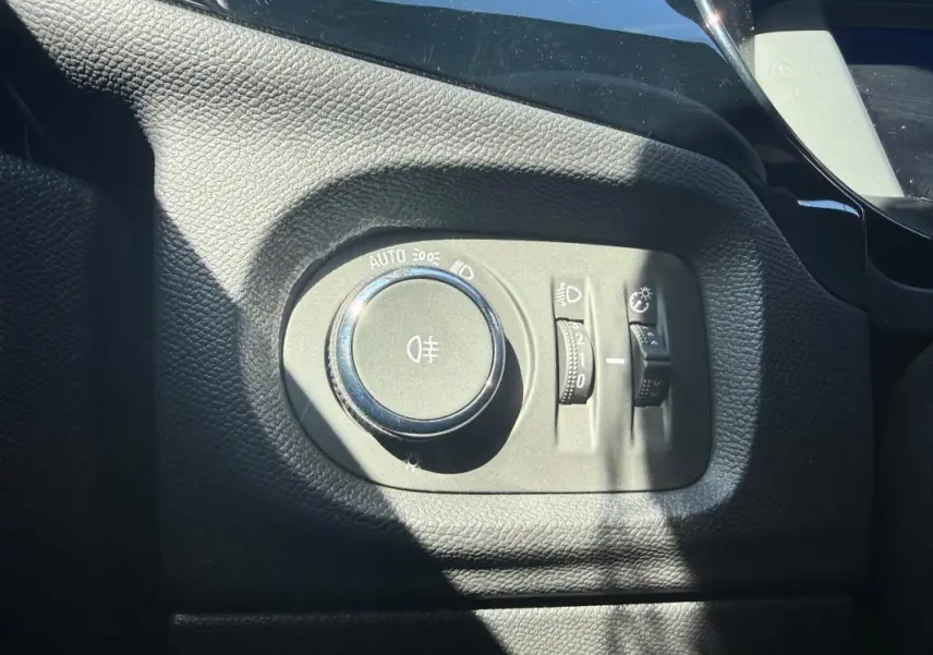 Gros plan sur la commande des phares et réglages d’éclairage dans l’habitacle noir de l’Opel Corsa rouge 2025.