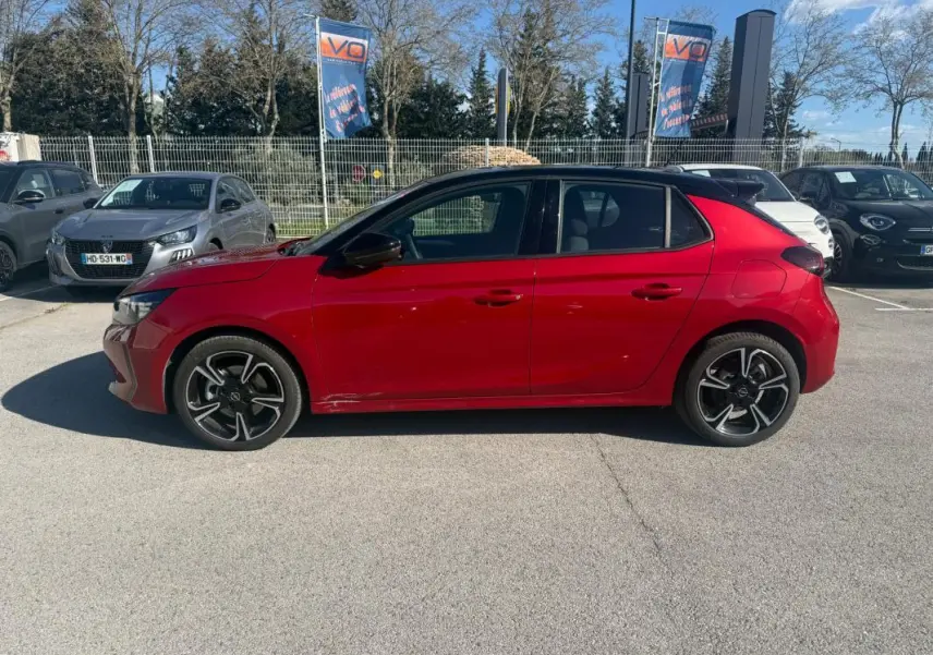 Vue latérale côté gauche d'une Opel Corsa rouge 2025 avec jantes noires et toit noir en concession.