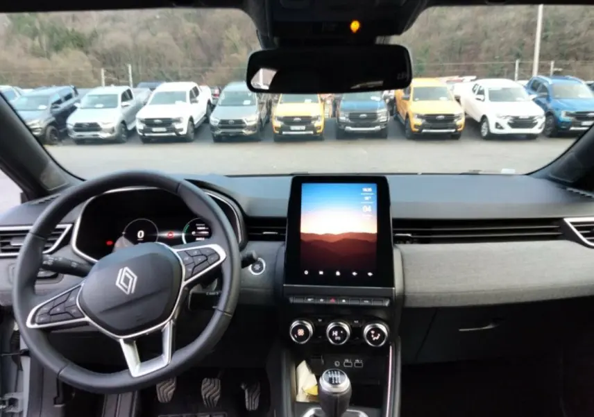 Vue intérieure avant de la Renault Clio gris rafale 2025, volant multifonctions et écran tactile vertical au centre.