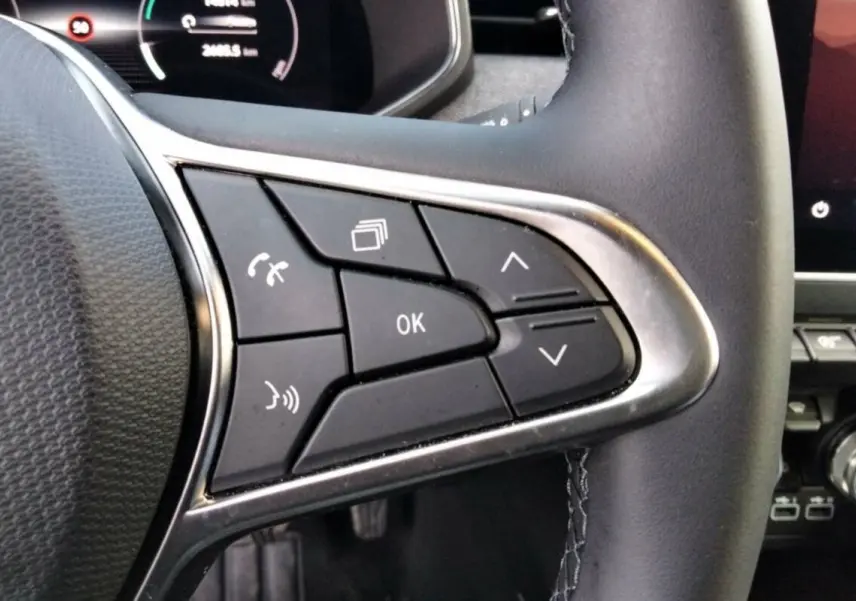 Gros plan sur les commandes multifonctions à droite du volant cuir de la Renault Clio gris rafale, tableau de bord numérique en arrière-plan.