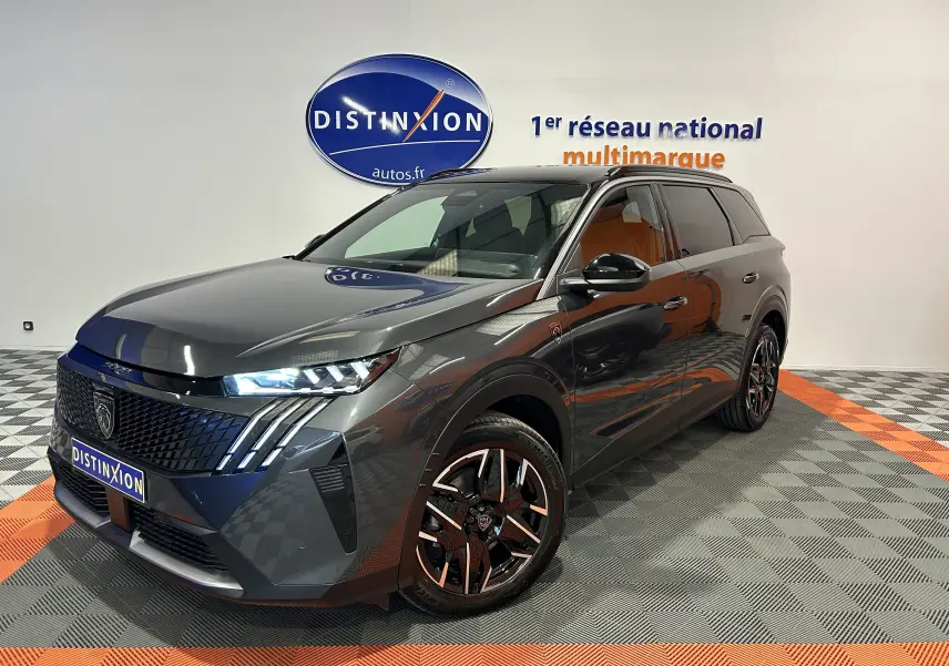 Peugeot 5008 Hybrid gris titane en 3/4 avant droit, avec jantes noires et phares LED allumés.