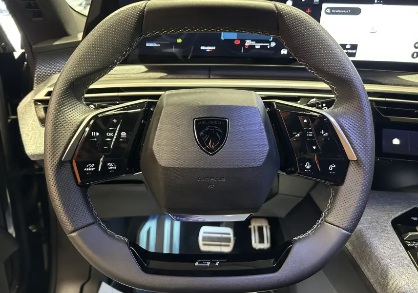 Vue rapprochée du volant cuir perforé gris du Peugeot 5008 Hybrid 2025 avec logo lion et inscription GT.