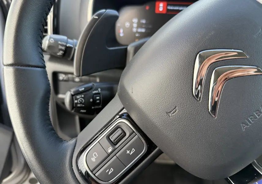 Gros plan sur le volant cuir noir du Citroën C5 Aircross 2024 avec commandes intégrées et logo chromé central.