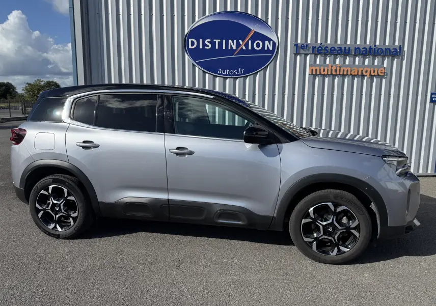 Profil droit d'un Citroën C5 Aircross 2024 gris Artense avec toit noir et jantes noires à motif géométrique.