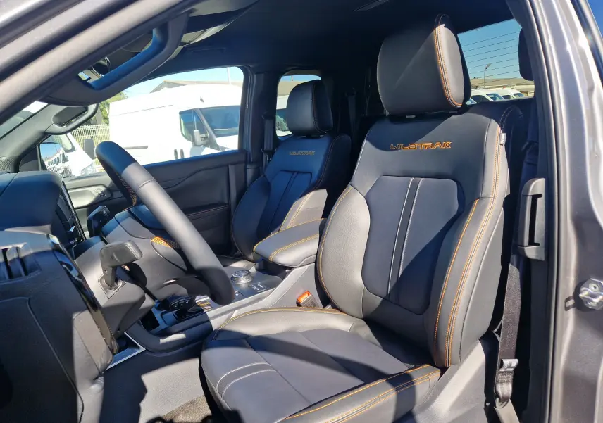 Vue intérieure côté conducteur du Ford Ranger Super Cabine Wildtrak 2026, sièges cuir gris carbone avec surpiqûres orange et logo Wildtrak brodé.