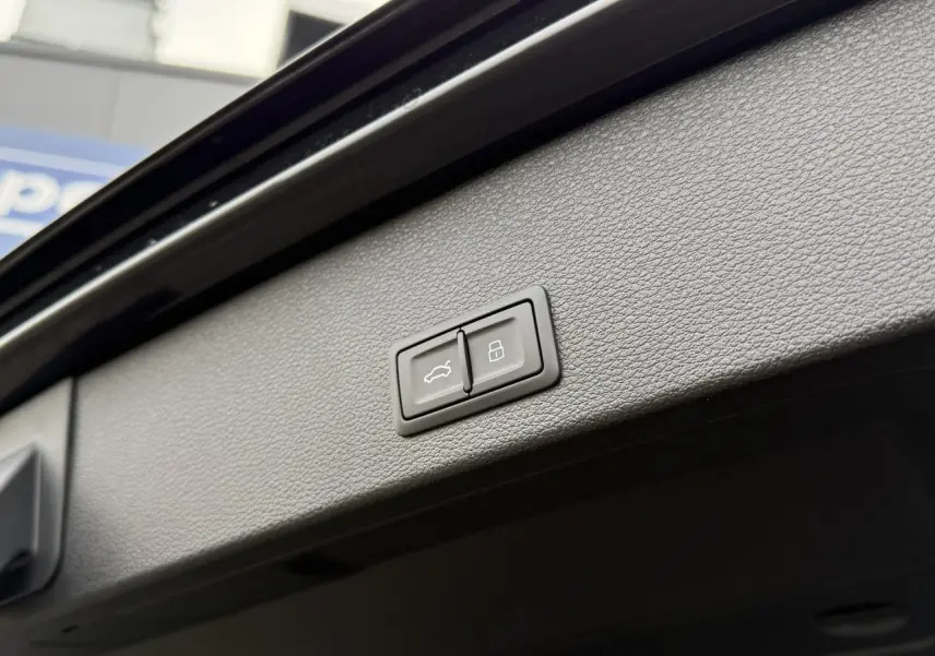 Boutons de commande du hayon électrique et de verrouillage intégrés dans le panneau intérieur noir du coffre d'un Audi Q2 noir métallisé.