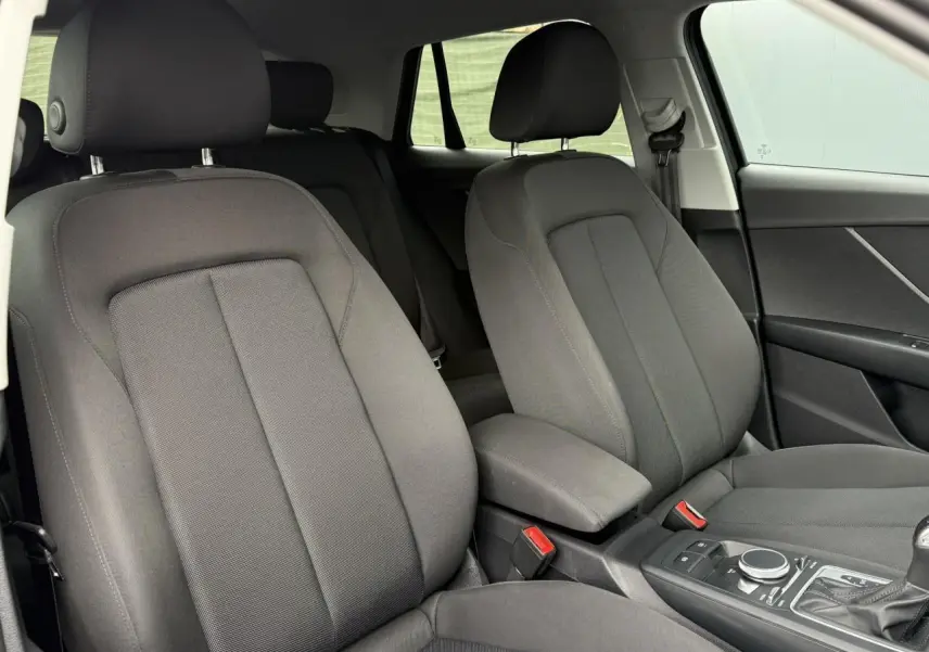Intérieur de l'Audi Q2 2023 en vue rapprochée des sièges avant en tissu gris avec console centrale et levier de vitesses automatique.