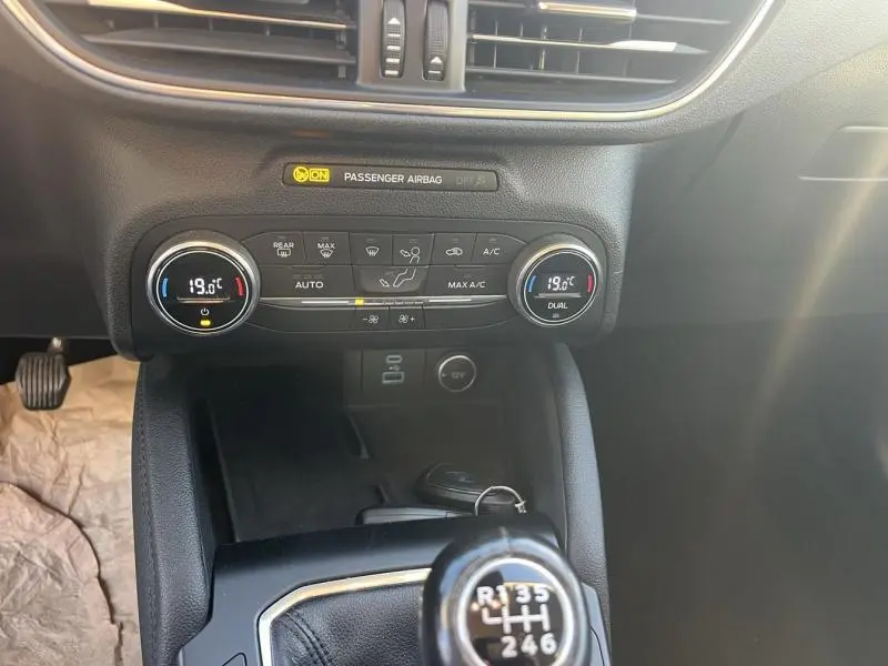 Vue rapprochée du tableau de bord et de la console centrale noire du Ford Kuga gris, avec commandes climatisation et levier de vitesse manuel.