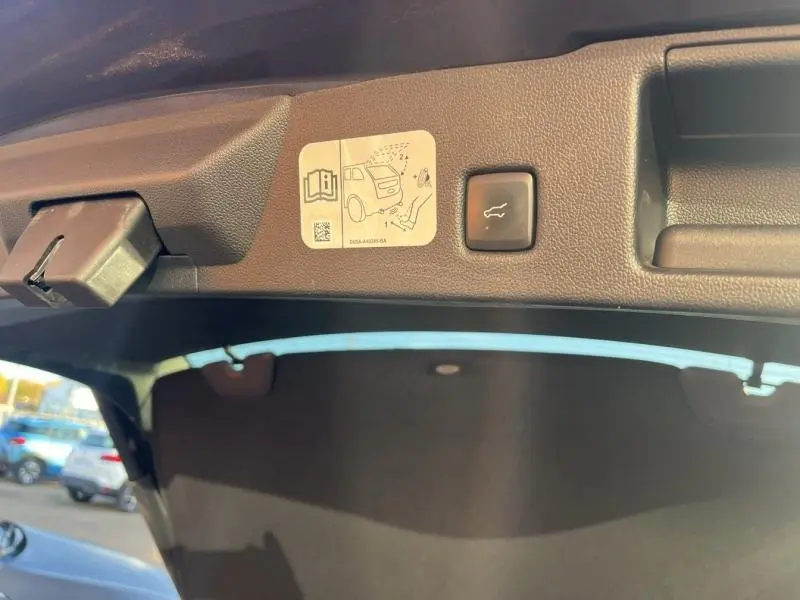 Détail du hayon intérieur gris métallisé du Ford Kuga 2021 avec bouton d'ouverture électrique et notice de sécurité.