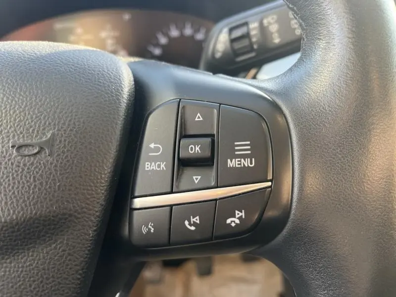 Gros plan sur les commandes multifonctions noires du volant cuir du Ford Kuga 2.0 EcoBlue 2021, intérieur gris.