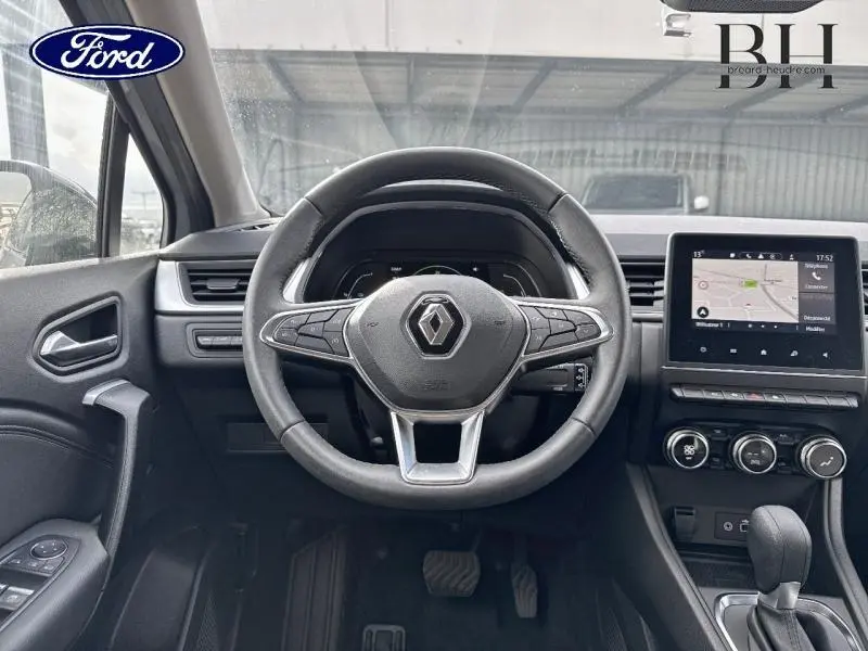 Vue intérieure centrée sur le volant Renault Captur 1.6 E-Tech gris Highland, avec écran tactile et commandes au volant visibles.