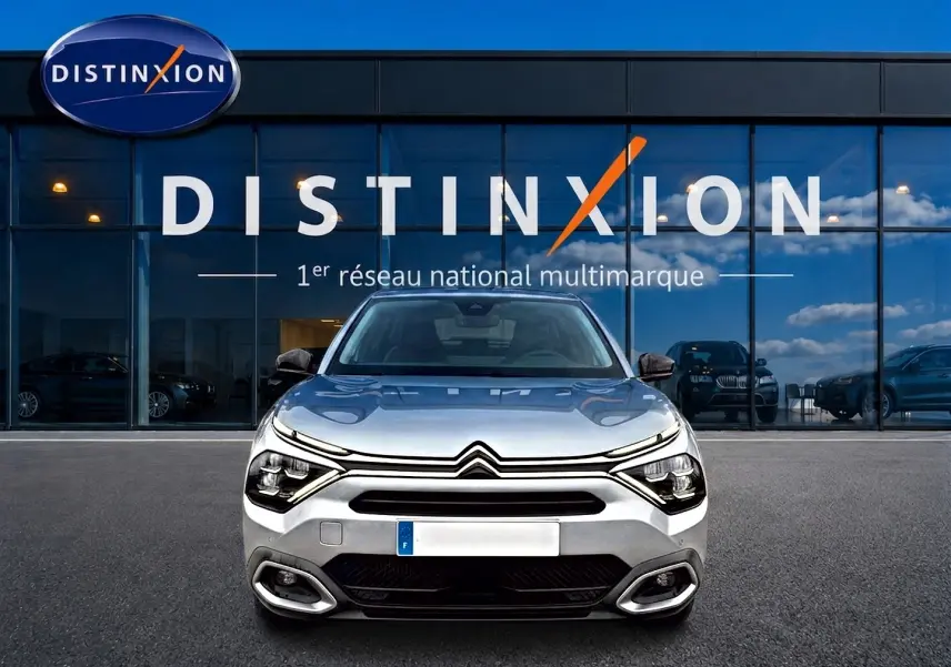 Vue frontale d'une Citroën C4 gris métallisé 2024 avec phares LED et calandre distinctive, devant un showroom Distinxion.