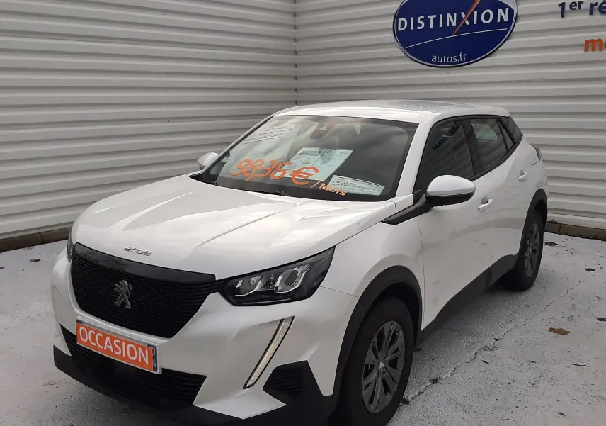 Peugeot 2008 blanc en 3/4 avant droit, avec calandre noire et feux LED, stationné devant un mur gris.