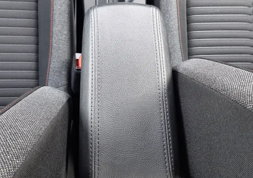 Vue plongeante sur l'accoudoir central en cuir noir et les sièges tissu noir avec surpiqûres rouges d'un Peugeot 2008 blanc.