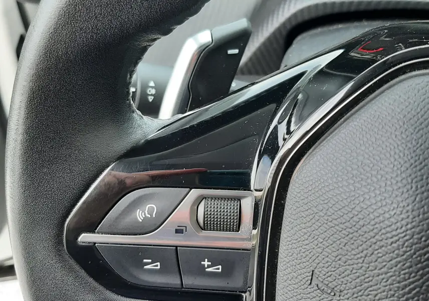 Gros plan sur la partie gauche du volant noir du Peugeot 2008 blanc, avec commandes audio et palettes de vitesse visibles.