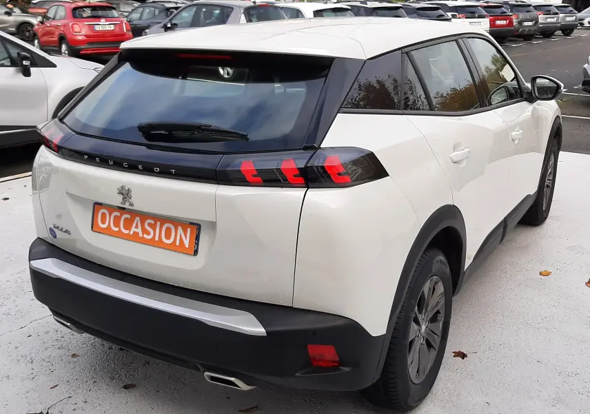 Vue 3/4 arrière droite d'un Peugeot 2008 blanc avec feux arrière LED et plaque "OCCASION" sur parking.