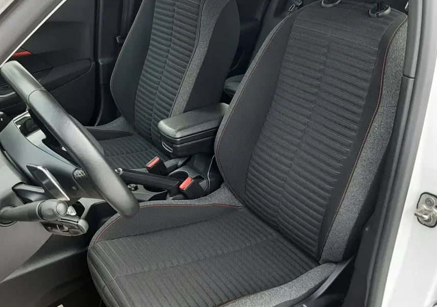 Vue intérieure côté conducteur du Peugeot 2008 blanc 2021, sièges tissu noir avec surpiqûres rouges et accoudoir central.