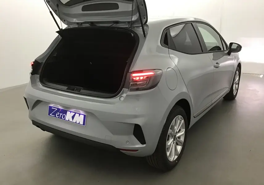 Vue 3/4 arrière droite d'une Renault Clio V gris Rafale avec coffre ouvert et feux arrière allumés dans un studio.